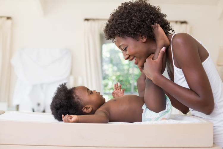 African-american woman looking at her baby smiling while changing their diaper.