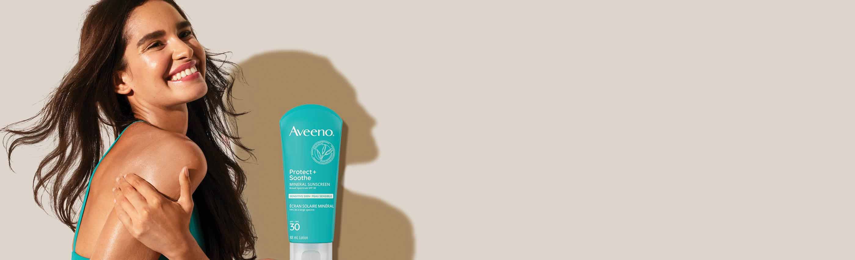 Close up profile of a woman with long brown hair smiling and AVEENO® SPF 50 mineral sunscreen for face, squeeze tube,  88 mL 