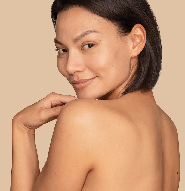 Woman with a bare back looking over her shoulder against a beige backdrop 